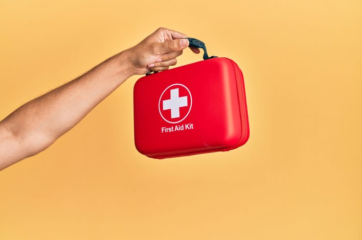 Hand of hispanic man holding first aid kit over isolated yellow background.